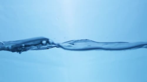 Waves of crystal clear blue mineral water, creating some tiny bubbles and droplets of in a water tan