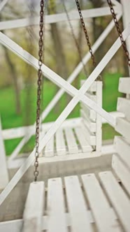 Extreme close up of a metal chain attached to a white wooden swing bench, showing rust details and t