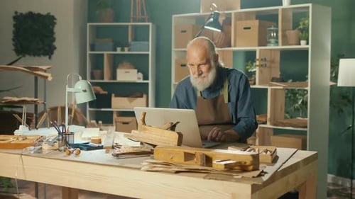Senior Man Using Laptop in Woodworking Workshop