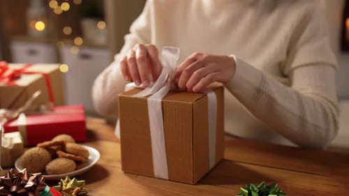 Woman opening gift box with white ribbon indoors