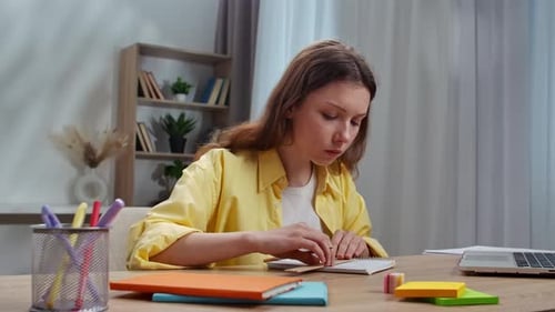 Focused Young Woman Writing in Notebook at Desk