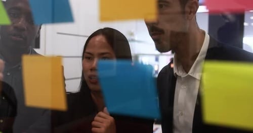 Multiracial colleagues working inside business office with glass walls and adhesive note