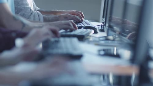 Junge Leute gemischter Abstammung sitzen in einer Reihe und arbeiten an Computern. Tippen auf der Tastatur.