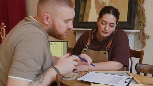 Gen Z Managers Discussing Menu of Drinks, Prices and Business Papers in Cafe