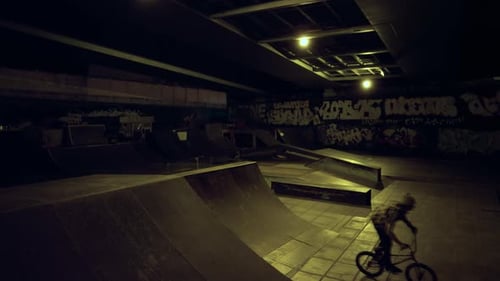 Un homme sportif fait une cascade dangereuse sur un vélo BMX en faisant du skate de nuit