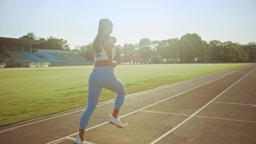 Beautiful Fitness Woman in Light Blue Athletic Top and Leggings Jogging in a Stadium. She is Runnin