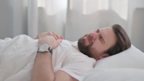Vue latérale d'un jeune homme adulte mal à l'aise qui essaie de dormir dans son lit