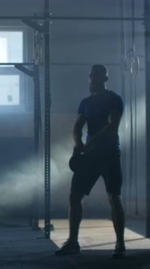 Silhouetted Athlete Performing Powerful Kettlebell Swings in Dimly Lit Industrial Style Gym with