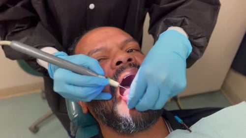 A close-up view of a middle aged man with a beard at the dentist. The mixed race man is getting his