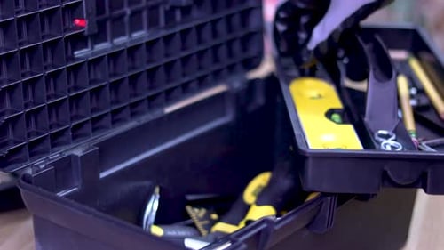 Eine Nahaufnahme eines Werkzeugkastens voller Werkzeuge. Eine Hand eines Handwerkers öffnet es und holt ein paar Werkzeuge heraus