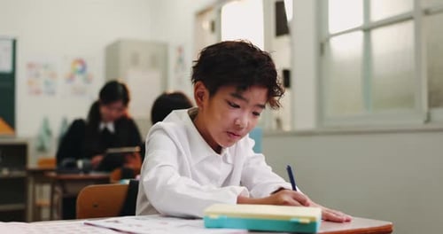 Boy, child and writing test in classroom, studying and notes for knowledge or education in Japan