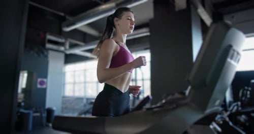 A Young Beautiful Woman in Sportswear is Training and Exercising on a Treadmill in a Gym