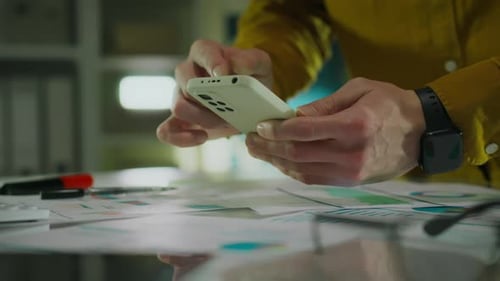 At the company office, a business analyst carefully studies the performance report. A smartphone