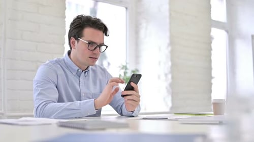 Young Man Celebrates Success on Smartphone in Office