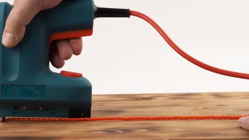 Close-up of a man's hand holding an electric stapler and fastening rope to a board.