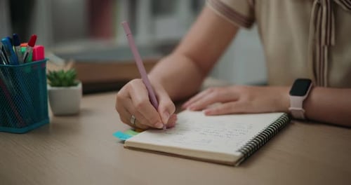 Woman Writes in Notebook at Desk with Pens