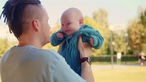 Young Father Holding His Newborn Baby in His Arms in the Park