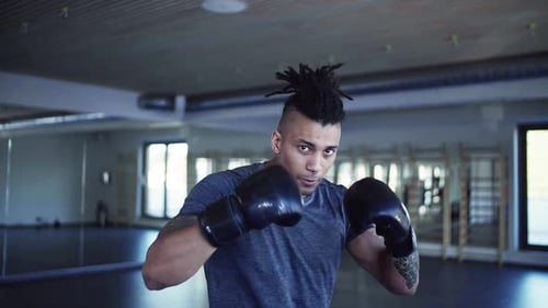 Young man with dreadlocks exercises boxing in a dark gym for fitness