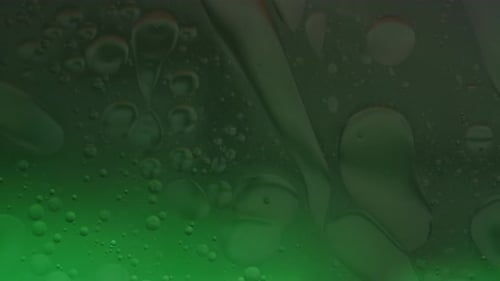 Grünes Wasser bei schwachem Licht mit glänzenden Öltropfen, die auf der Oberfläche schwimmen und sich langsam vermischen abstrakter Hintergrund