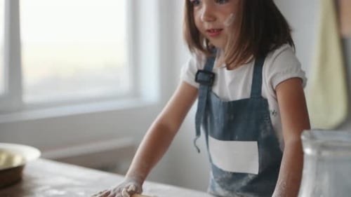 Close up view of kid in chef uniform that kneading the dough by wooden tool on the kitchen