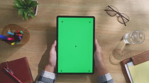 Top down view of man's hands holding a mock up green screen tablet on a desk