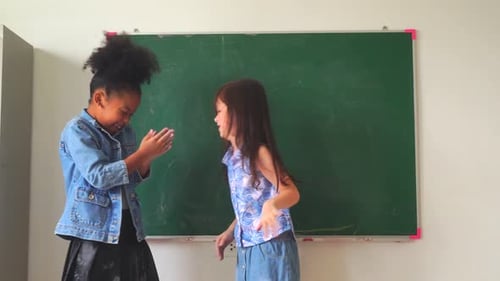 Two Cheerful Girls Touching Hands Near Chalkboard