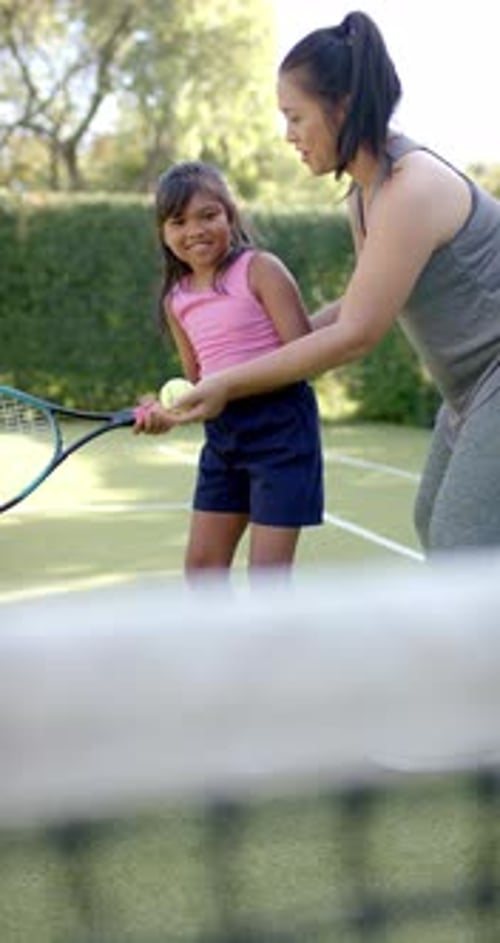 Vertical video: Teaching tennis, woman helping girl with racket on outdoor court