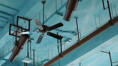 Ventiladores de techo y tubos contra un techo industrial azul claro.