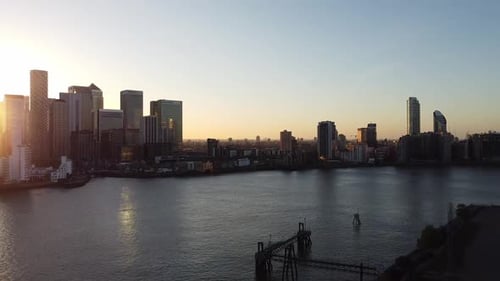 Cinematic aerial shot of Canary Wharf district with skyscrapers beside River Thames during sunset in