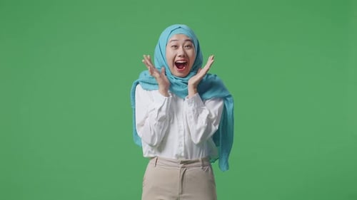 Femme musulmane asiatique souriant et disant « Wow » debout sur le fond d'écran vert