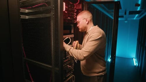 Man Connecting Cables in Dark Server Room