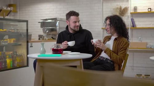 Young Caucasian Man and Woman Drinking Tea Talking Dating in Cafe in Urban City Positive Relaxed