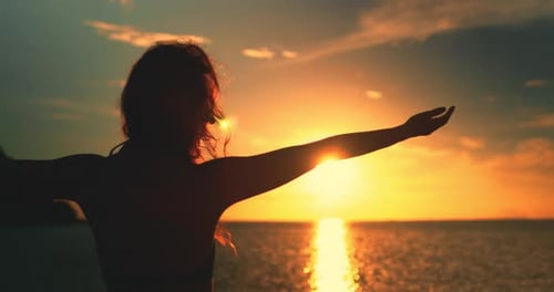 Mädchen erhobene Hände genießen den strahlenden Sonnenuntergang am Meer