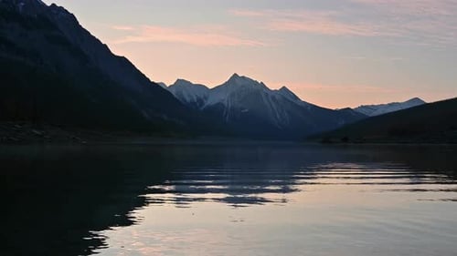 Stunning Sunset Over Calm Lake Water Reflecting Snow Capped Mountains