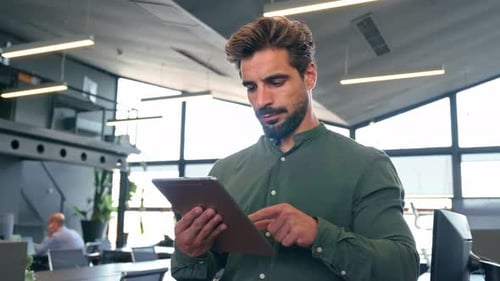 Smiling Busy Young Latin Business Man Using Tablet Standing in Office