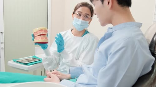 Asian female dentist explaining teeth care to a male patient in a dental clinic.