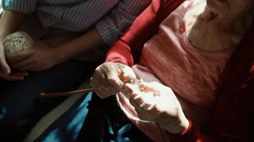 Senior Woman Knitting Next to a Young Adult