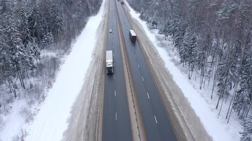 A white truck drives along the road among snowy trees in cold winter.