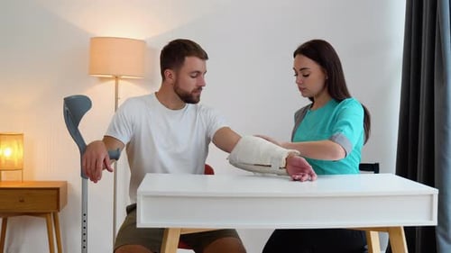 Doctor Examines Arm Cast of Young Adult Man