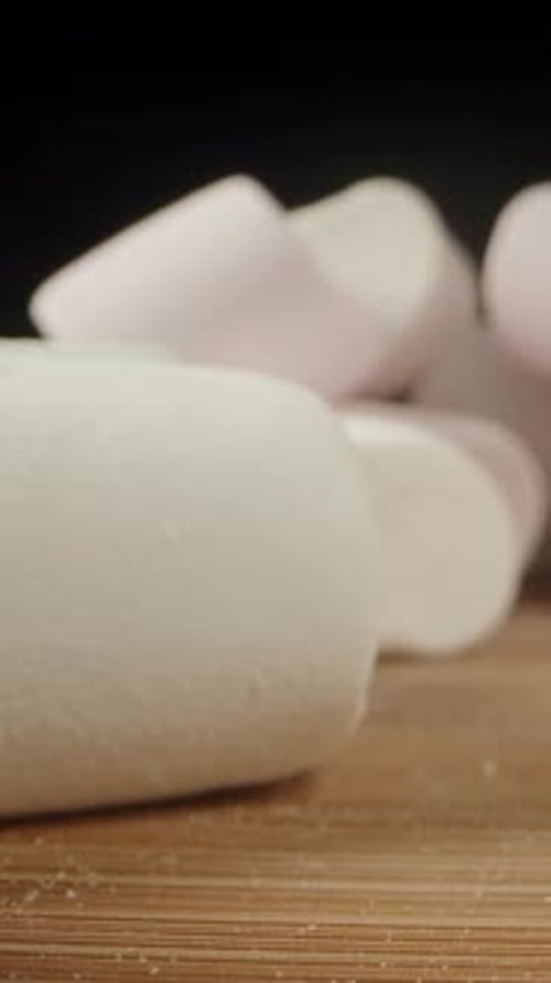 Marshmallows of different colors are scattered on the table. Dolly slider extreme close-up. Vertical