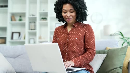 Young african american female freelancer typing on laptop while sitting on sofa at home office.