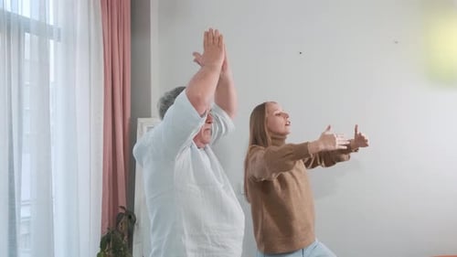 Senior Man and Young Woman Doing Yoga Indoors