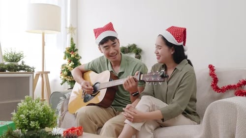 Couple in Santa Hats Playing Guitar at Christmas