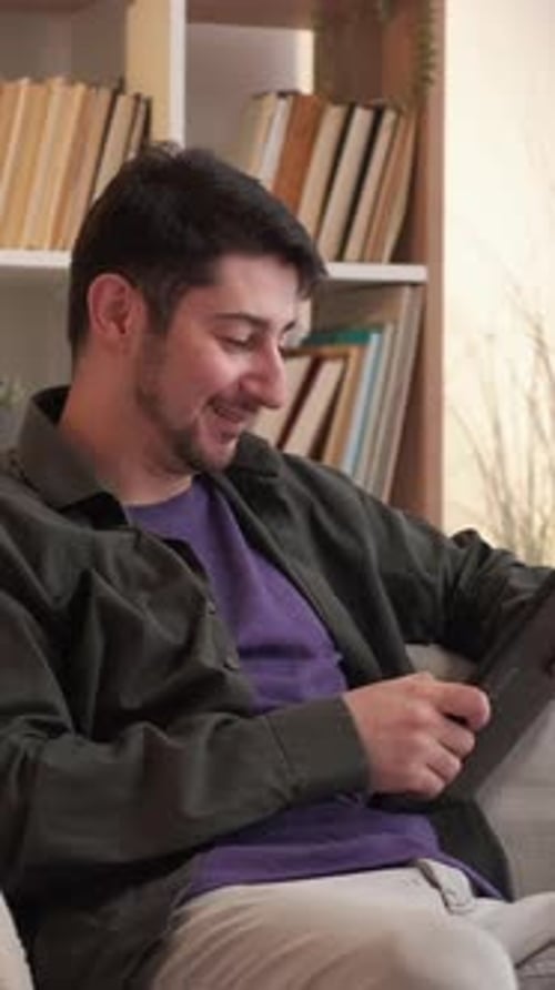 Smiling Man Using Tablet Device on Couch Indoors