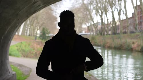 Young man walking under bridge during winter season wearing coat and scarf