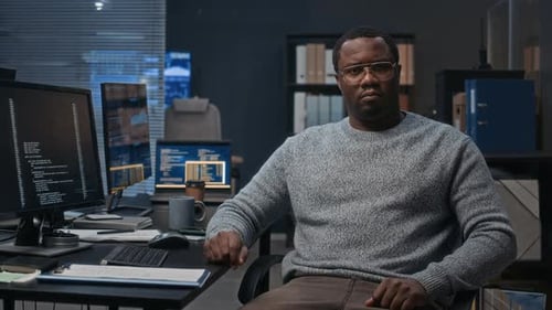 Man Sits in Office with Computer Code on Screen