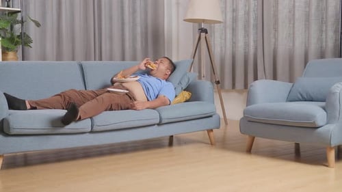 Adult Man Lying on Couch Eating Burger
