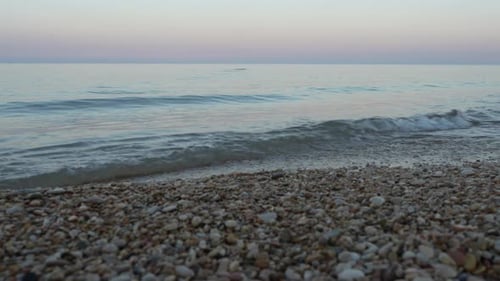 Small wave breaking on pebble beach under pastel sky in Adriatic Sea