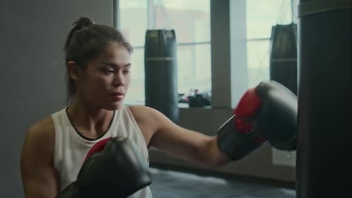 Muscular Hispanic Female Boxer Practicing on Punch Bag at Gym