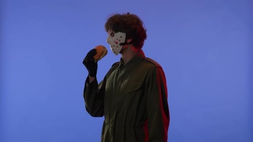 Man in White Mask Sniffing a Burger and Pointing His Finger in the Direction on Blue Background with